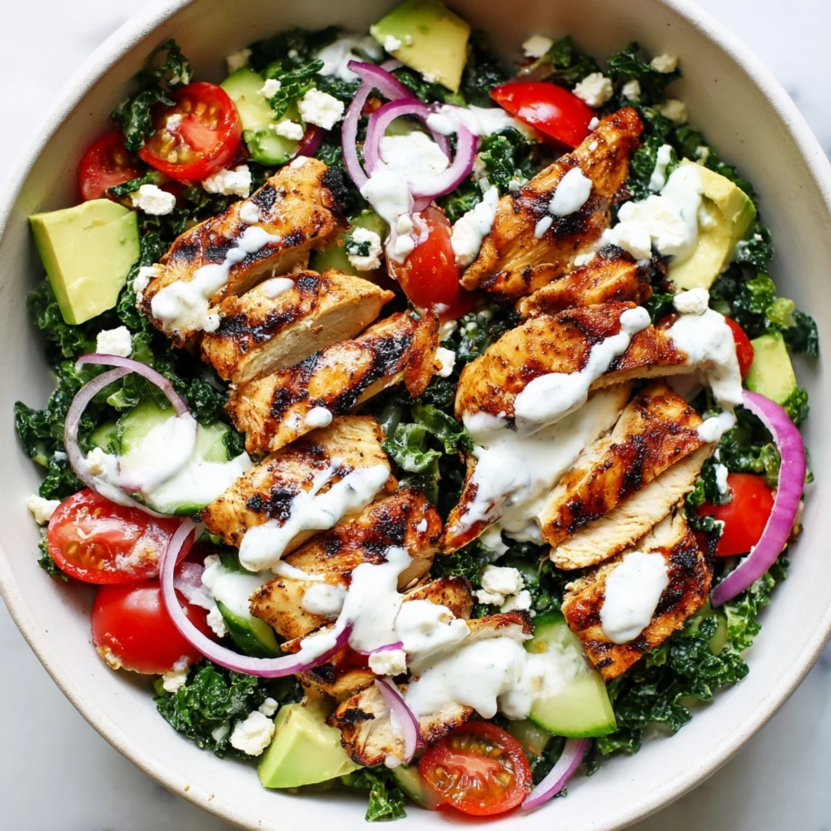 Sliced grilled chicken served over massaged kale with tomatoes, cucumber, and creamy feta