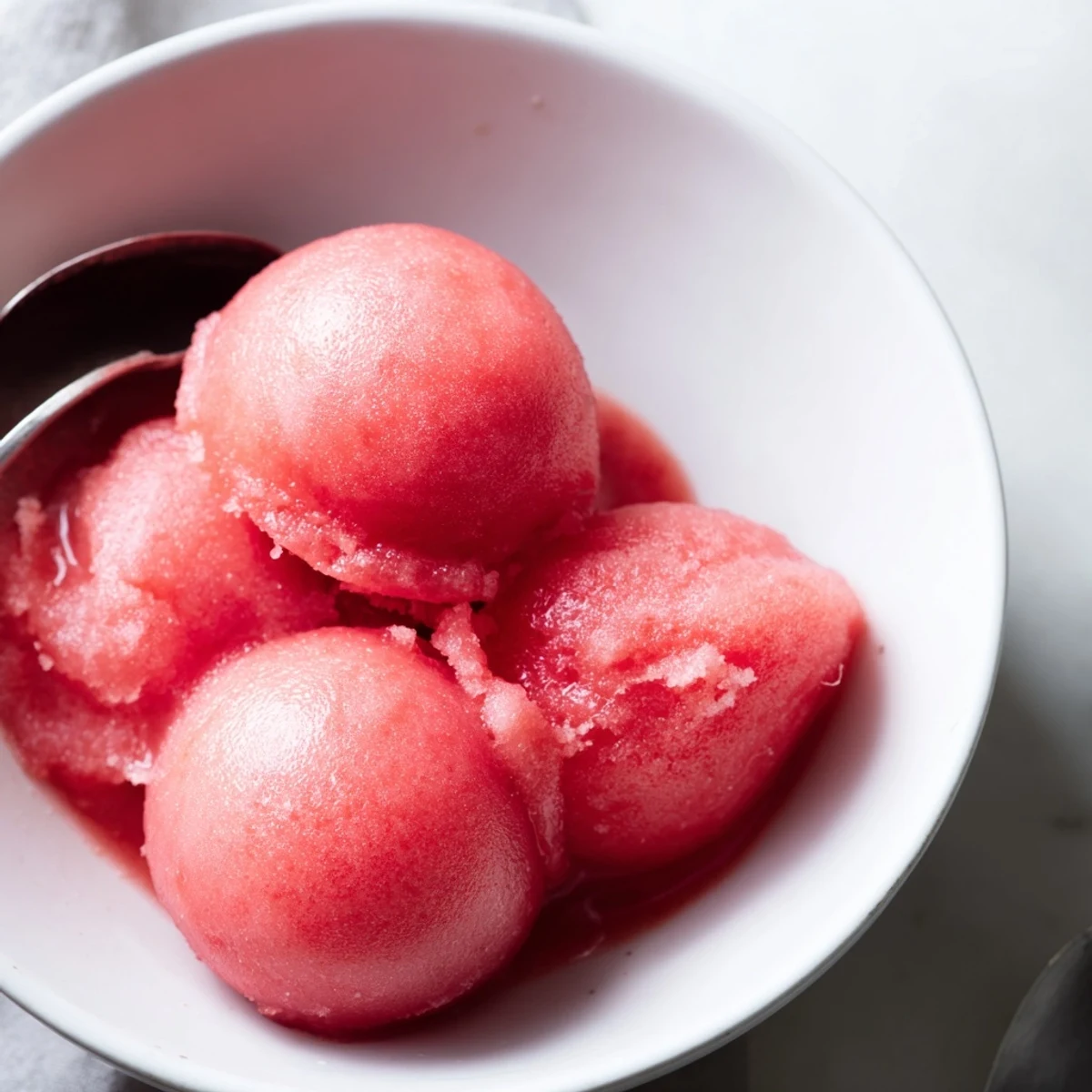 Creamy watermelon sorbet melting slightly in a white ceramic bowl with mint sprigs