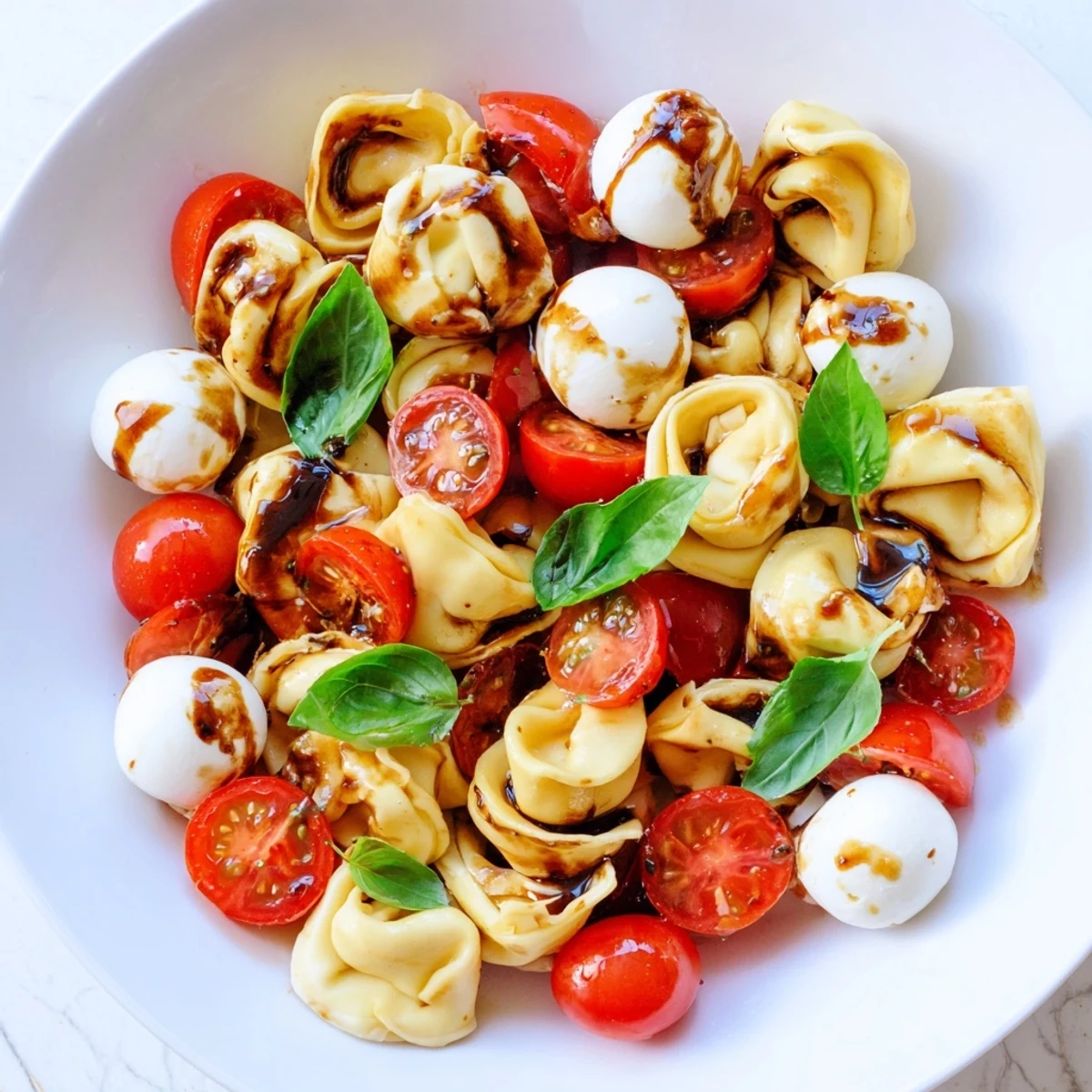 Colorful Tortellini Caprese Salad tossed with cherry tomatoes, fresh mozzarella, and basil in balsamic glaze
