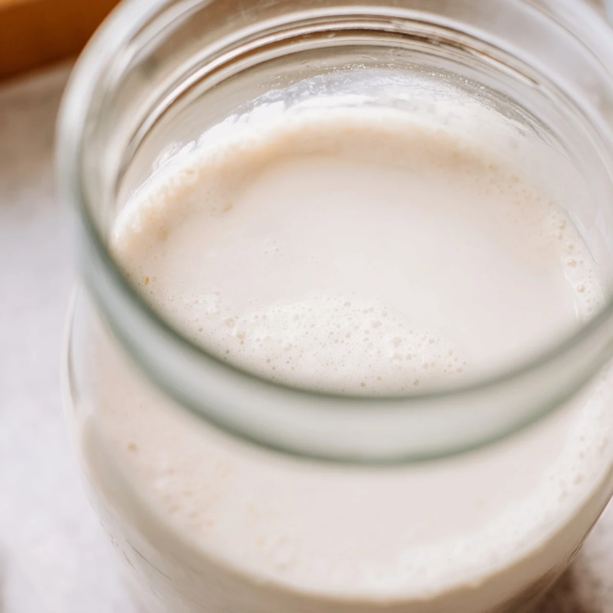 Fresh homemade almond milk being poured into a clear glass pitcher showing its smooth dairy-free consistency