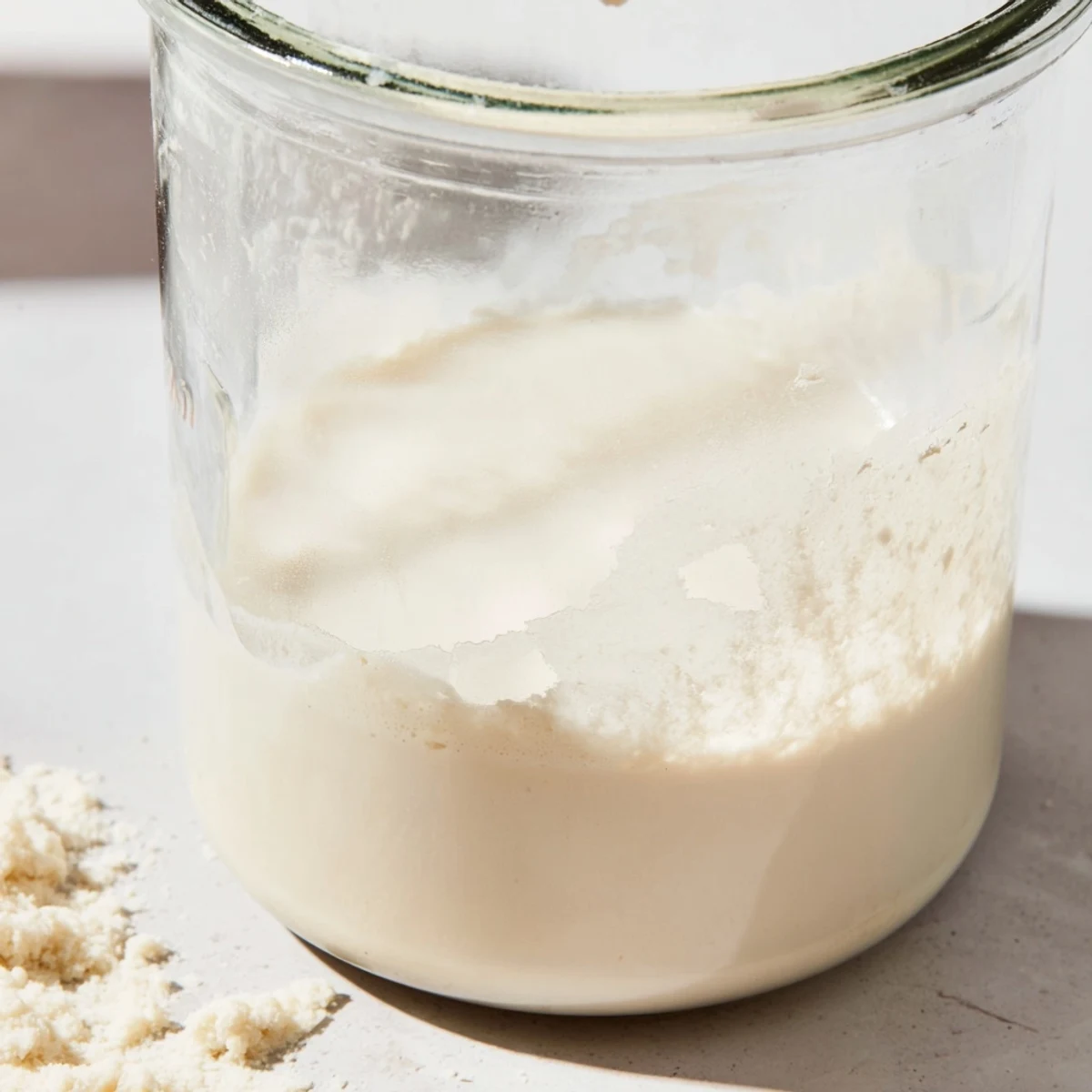 Creamy homemade almond milk stored in a mason jar alongside raw almonds on a marble surface