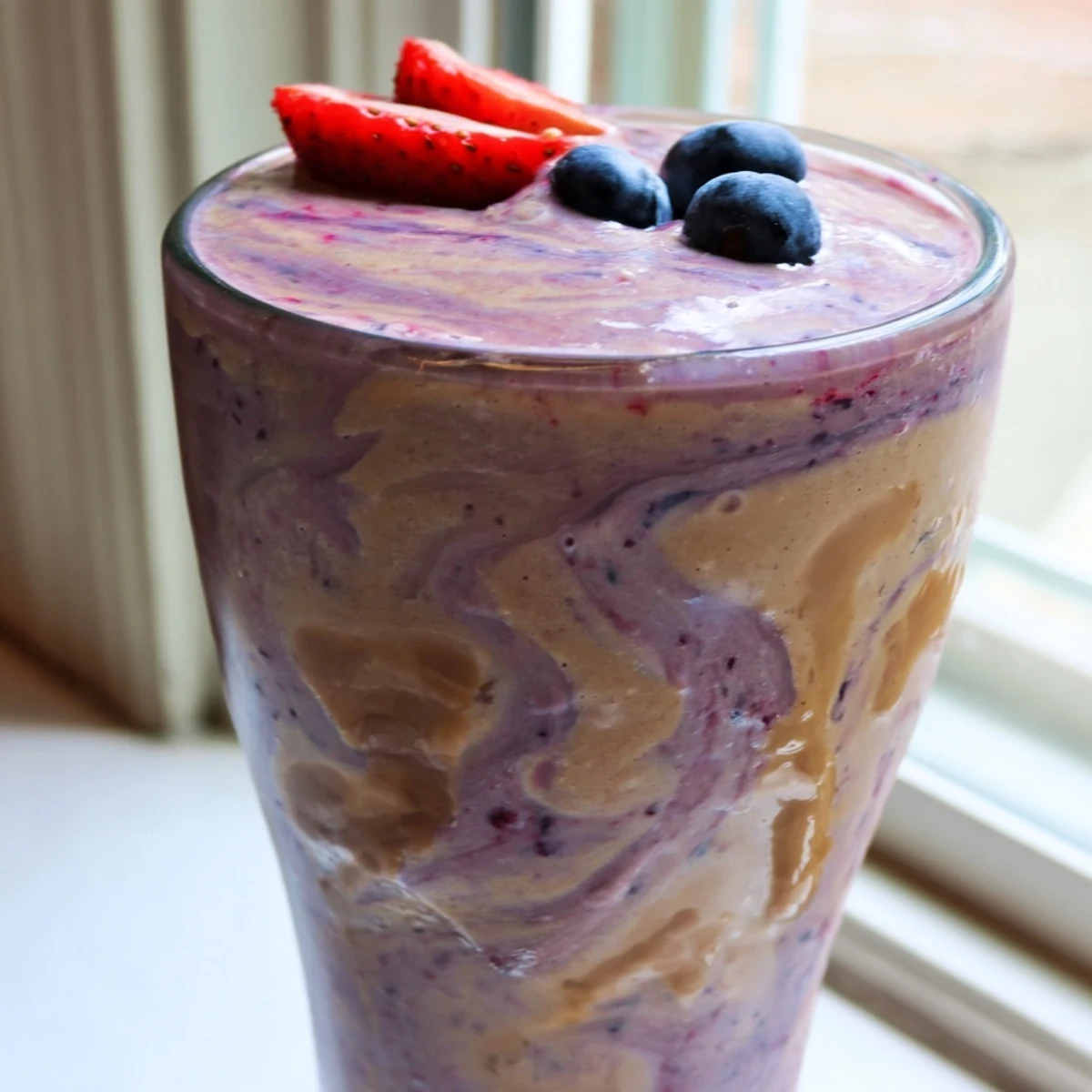 Thick purple peanut butter berry smoothie topped with fresh strawberries in a glass