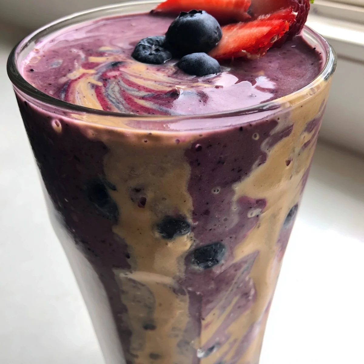 Rich peanut butter berry smoothie swirled with berry specks served in two tumblers