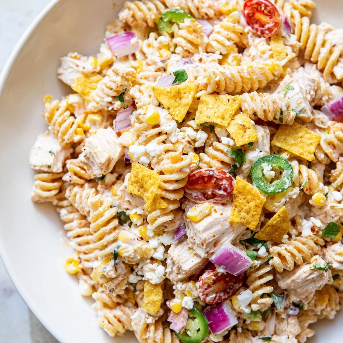 Vibrant elote-style chicken pasta salad loaded with charred corn, ripe tomatoes, and zesty lime crema
