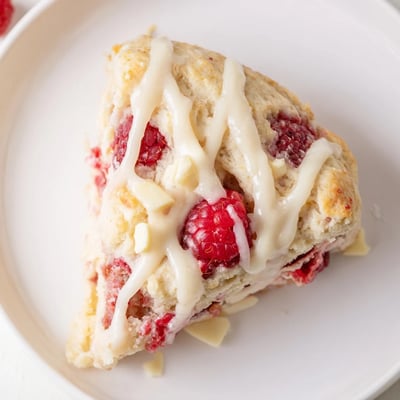 Warm Raspberry White Chocolate Scones with Glaze drizzled over the top, served on a rustic wooden board for breakfast or brunch.