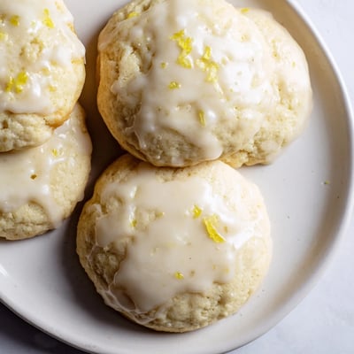 A close-up of soft, cake-like Lemon Ricotta Cookies drizzled with sweet-tart lemon glaze, ready to serve with coffee.